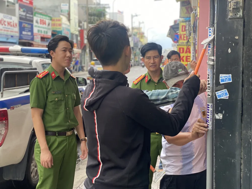 Công an đưa các đối tượng dán tờ rơi đi bóc gỡ quảng cáo do mình dán
