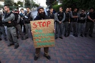Israeli police officers watch a left-wing activist as he holds a placard that reads Stop the settlement in East Jerusalem during a protest against Jewish settlement in the Sheikh Jarrah neighbourhood in East Jerusalem April 23, 2010. Israeli police officers watch a left-wing activist as he holds a placard that reads Stop the settlement in East Jerusalem during a protest against Jewish settlement in the Sheikh Jarrah neighbourhood in East Jerusalem April 23, 2010.