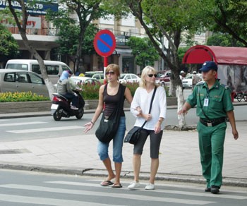 A volunteer (R) of the Tourist Information Center helps foreign visitors cross a street in the heart of HCM City. (Photo: KK) A volunteer (R) of the Tourist Information Center helps foreign visitors cross a street in the heart of HCM City. (Photo: KK)