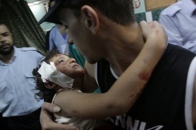 A man carries a wounded young child into a hospital following Israeli air strikes on Gaza City on July 30, 2010.