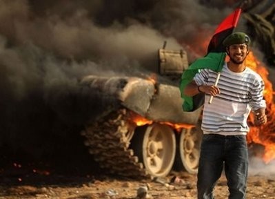 AFP - A Libyan rebel holds the Kingdom of Libya flag as he walks past a burning tank bombed by the coalition air force in the town of Ajdabiya. AFP - A Libyan rebel holds the Kingdom of Libya flag as he walks past a burning tank bombed by the coalition air force in the town of Ajdabiya.
