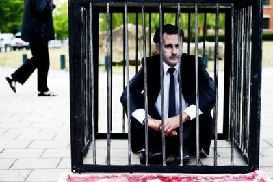 A protester wearing a mask of Syrian leader Bashar al Assad sits on the ground inside a cage outside the International Criminal Court (ICC) in The Hague, on June 7, 2011 A protester wearing a mask of Syrian leader Bashar al Assad sits on the ground inside a cage outside the International Criminal Court (ICC) in The Hague, on June 7, 2011