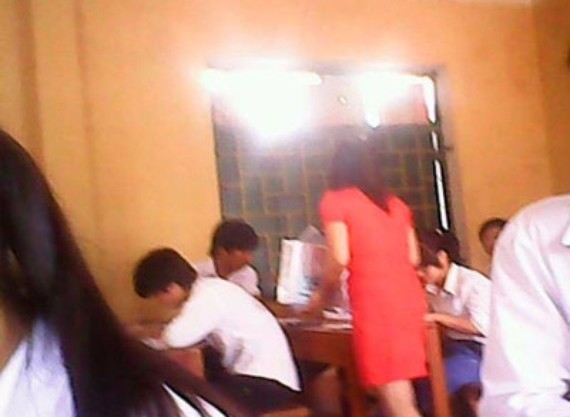 One clip shows a woman in a red dress collecting answer cheat sheets from students prior to end of examination time One clip shows a woman in a red dress collecting answer cheat sheets from students prior to end of examination time