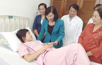Nguyen Thi Thu Ha (in blue, standing) presents a gift to Nguyen Thi Kim Thanh at the Tam Duc Heart Institute (Photo: SGGP)
