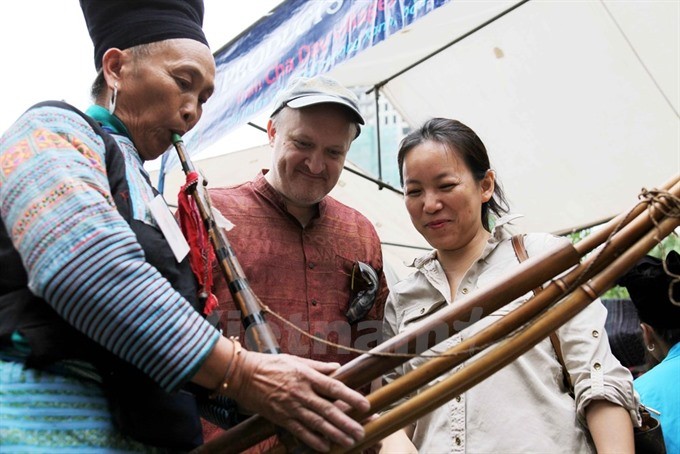 A local blows khèn (panpipe) as international tourists look on. — Photo vietnamplus.vn