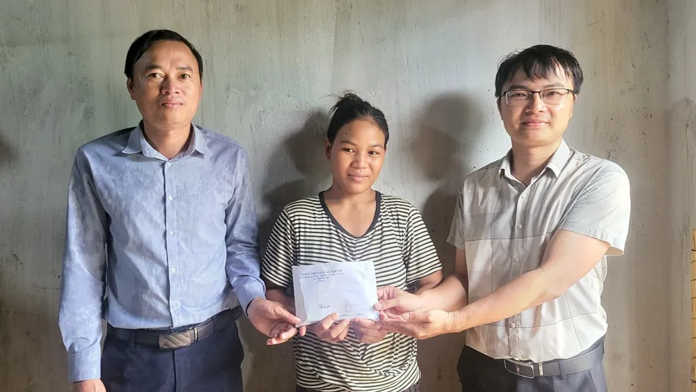 Ông Trần Thanh Minh, Bí thư Đảng uỷ (bìa trái) và ông Hà Đức Mỷ, Chủ tịch UBND xã Đắk Pxi trao số tiền bạn đọc Báo SGGP giúp đỡ chị Y Khổ