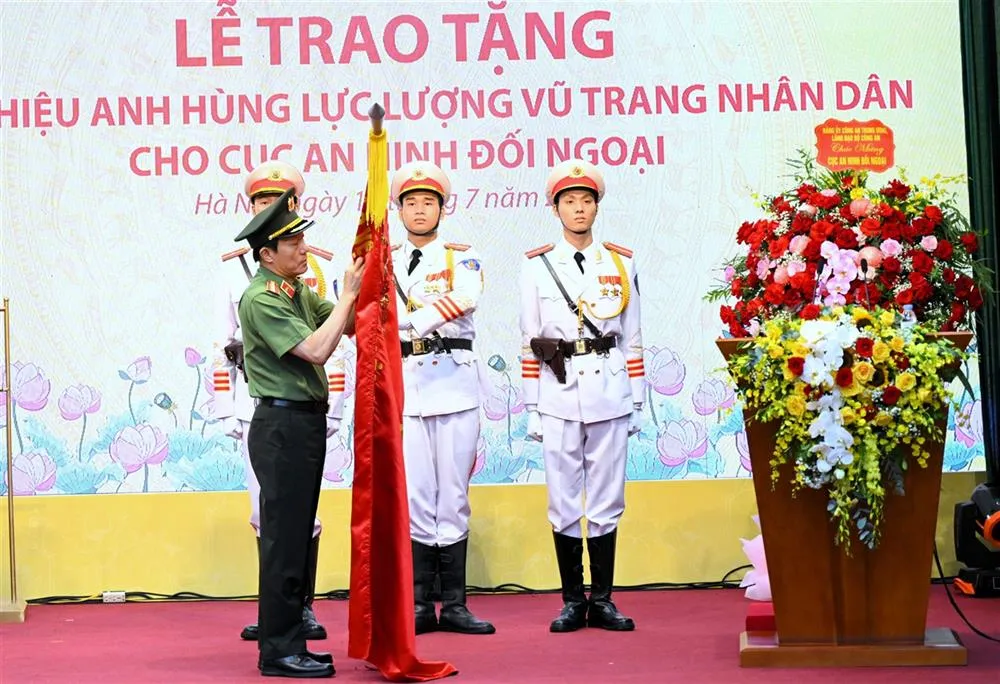 Bộ trưởng Lương Tam Quang trân trọng gắn danh hiệu Anh hùng lực lượng vũ trang nhân dân lên lá cờ truyền thống của Cục An ninh đối ngoại. Ảnh: Cổng thông tin Bộ Công an