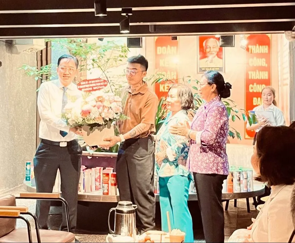 Bí thư Đảng ủy phường Phạm Ngũ Lão Lê Tấn Đạt (bìa trái) tặng hoa chúc mừng đại diện quán Caztus