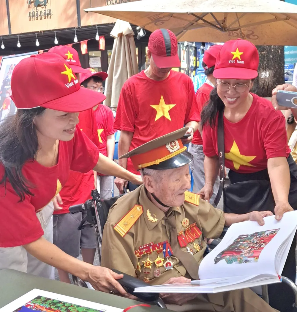 Ông Nguyễn Văn Thành, cựu chiến binh 98 tuổi, nhân vật trong một tác phẩm tại triển lãm sách ảnh "50 năm niềm vui thống nhất" Trien lam - 6.jpg