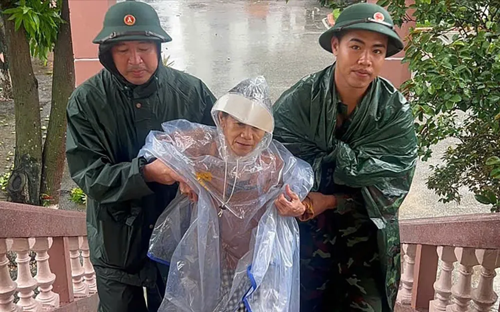 Bà Nguyễn Thị Tuệ (69 tuổi, trú phường Vinh Phú, tỉnh Nghệ An) được các chiến sĩ Lữ đoàn 80 (Quân khu 4) hỗ trợ đến nơi tránh trú bão. Ảnh: MINH HUY Z7a.jpg
