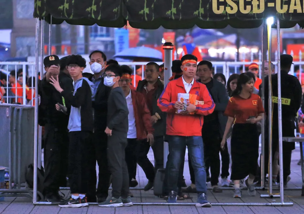 Càng sát giờ bóng lăn, dòng người đổ về sân Mỹ Đình rất đông. Người hâm mộ qua khỏi lớp kiểm tra an ninh đặt trước cổng sân để tiến vào bên trong. Dự báo 4 vạn chỗ ngồi sẽ được "phủ kín" khán giả.