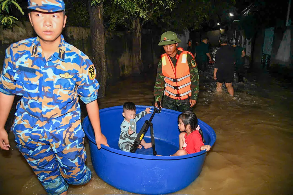 Các lực lượng hỗ trợ trẻ em ra khỏi vùng ngập sâu nguy hiểm. Ảnh: LỮ ĐOÀN 681 Các lực lượng hỗ trợ người trẻ nhỏ di dời ra khỏi vùng ngập sâu nguy hiểm.jpg