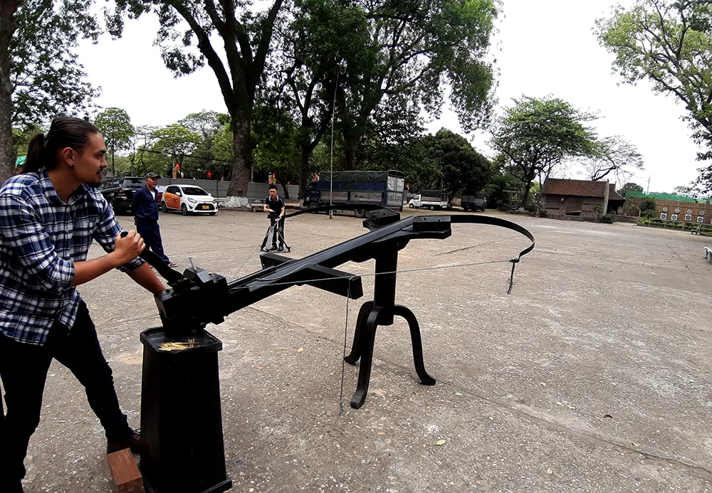 Andrei Ngo trải nghiệm bắn thử &quot;nỏ thần&quot; dưới sự hướng dẫn của kỹ sư vũ khí Vũ Đình Thanh. Ảnh: Lưu Thủy