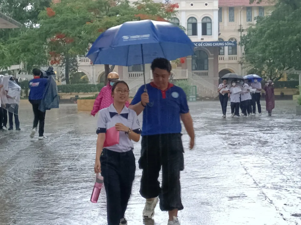 Một thí sinh được tình nguyện viên che dù rời khỏi điểm thi