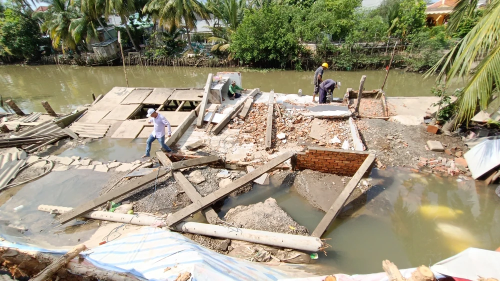 Tranh thủ thủy triều xuống, thực hiện tháo dỡ căn nhà bị sạt lở, khơi thông dòng chảy. Ảnh: LONG HẬU