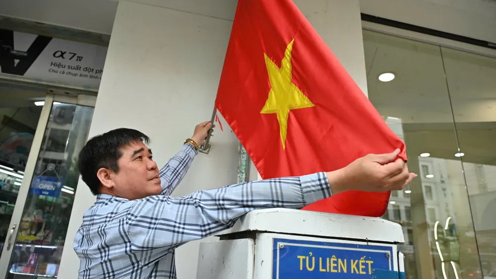 Ông Trần Văn Hưởng, ngụ tại số 90, đường Trần Hưng Đạo, phường Bến Thành chỉnh trang cờ Tổ quốc trước nhà. Ảnh: VĂN ANH Hinh 2.jpg