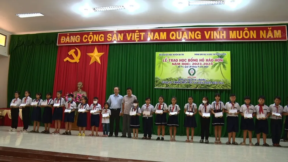 Ông Dương Minh Tùng, Chủ tịch UBND huyện Ba Tri (phải) và ông Trần Thanh Tuấn, Chủ tịch kiêm Giám đốc Công ty TNHH MTV XSKT Bến Tre (trái) trao học bổng cho các em học sinh
