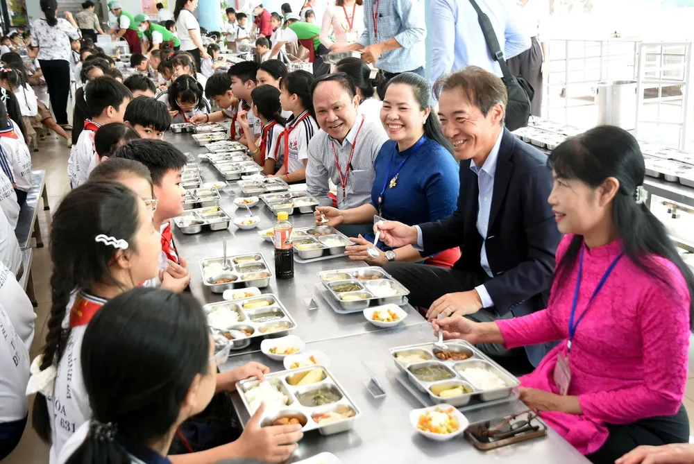 Ông Koichi Ozaki, Tổng Giám đốc Ajinomoto Việt Nam (mặc vest) dùng bữa trưa theo thực đơn của Dự án Bữa ăn học đường cùng học sinh. (Nguồn ảnh: A Lộc)