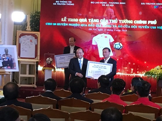 Prime Minister Phuc (L) presents a gift to a leader of poor district (photo: SGGP)