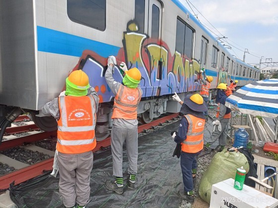 Workers use cleaning solvents to remove stains on the side of the carriage with colorful graffiti.