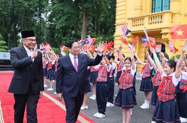 The two PMs wave at Vietnamese children at the welcome ceremony in Hanoi on July 20. (Photo: VNA)