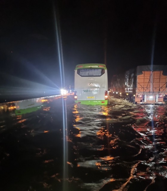 Trucks and passenger buses with high undercarriage clearance move slowly through flood water