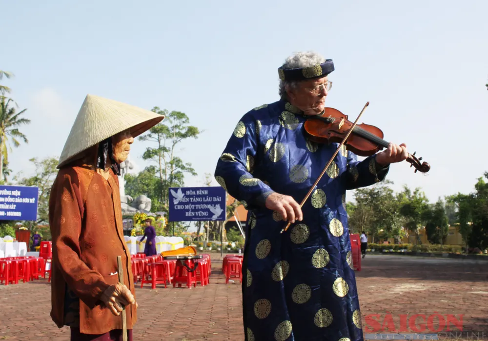 Ông Mike Boehm kéo cây vĩ cầm cho cụ bà Phạm Thị Trợ một điệu khúc. Bà Trợ thường gặp ông Mike Boehm khi ông trở về Sơn Mỹ. Trong vụ thảm sát Sơn Mỹ, bà có 2 người con bị thảm sát. Ảnh: NGUYỄN TRANG