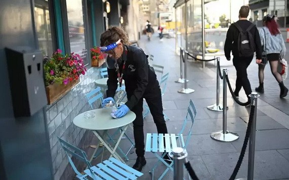 英國利物浦一名女服務員穿著防護設備清理餐桌。（圖源：AFP）