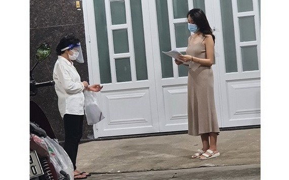 平盛郡第十九坊第三街區第四十六組長黎氏玉貝（左）挨家挨戶派發疫苗接種登記表。