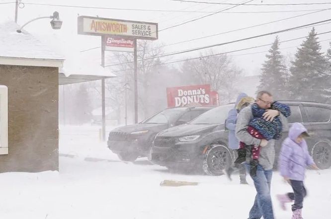 當地時間2022年12月23日，美國密歇根州，一場影響美國大部分地區的大規模冬季風暴中，一個家庭擠在一起，迅速向他們的汽車移動，以擺脫嚴寒。（圖：互聯網）