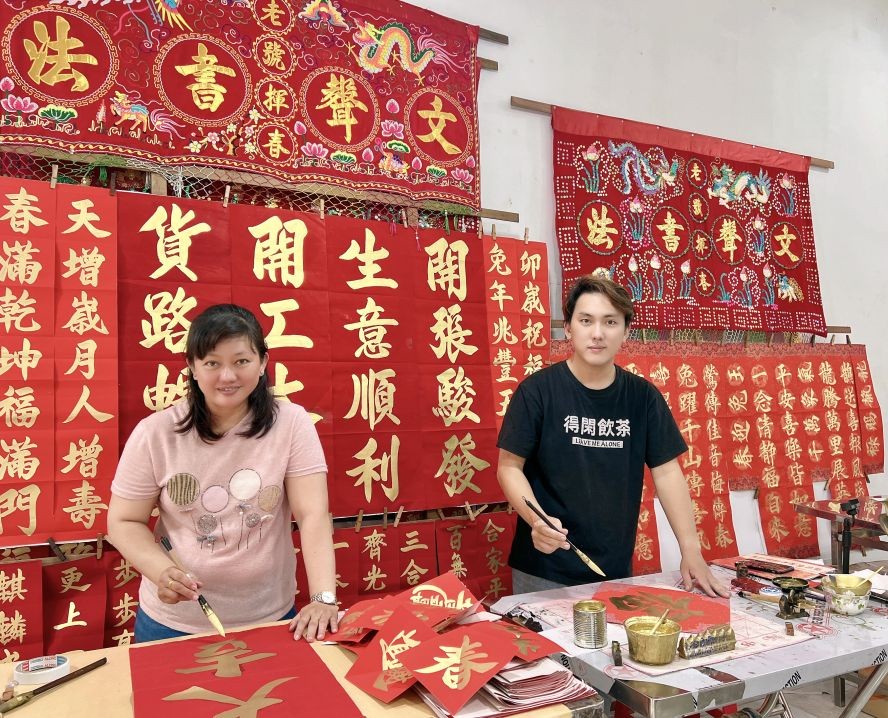 梁岱媮与梁朝铭正在挥毫挥春。