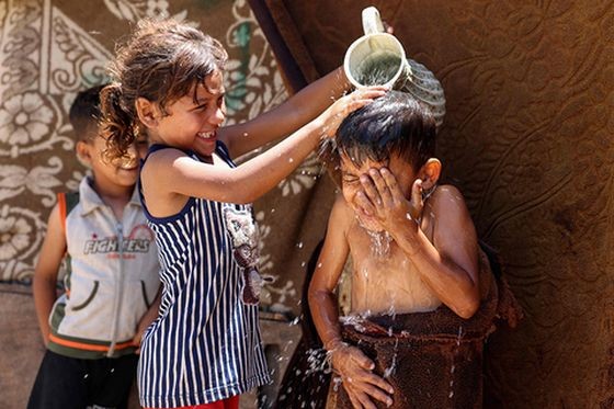 当地时间2023年7月18日，加沙城，炎热天气里，孩童们泼水降温。欧盟气候检测机构哥白尼气候变化服务的数据显示，7月的前三周是有记录以来最热的三周，并且本月有望成为最热的7月，也是有记录以来最热的一个月。（图：Mohammed Abed/视觉中国）