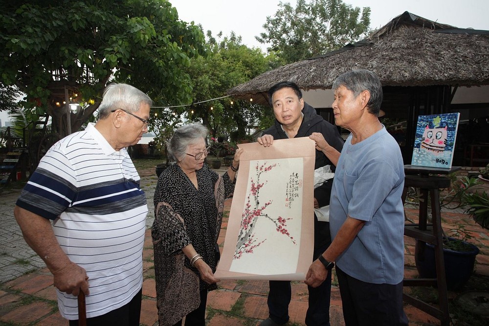 李克柔画家向戴显祖、阮氏心和黄献平（顺序右一至四）介绍戴顽君大师生前给他赠送的《红梅图》。