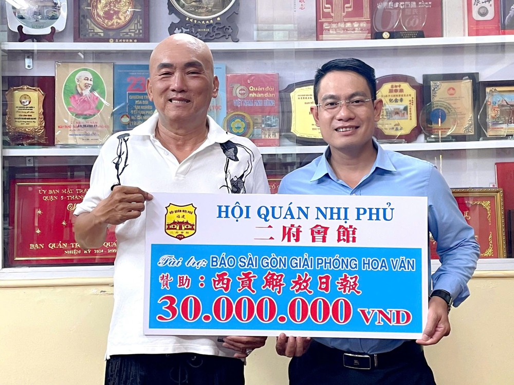 二府会馆理事赖学良（左）把3000万元赠报经费交给本报编委文忠孝。