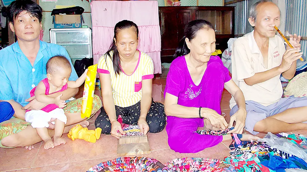 Vợ chồng chị Lợi (bên trái) và 2 hội viên khiếm thị đang học nghề đan thảm chùi chân tại nhà