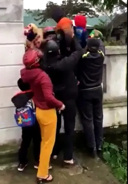 Đưa con đi học muộn, phụ huynh phải bế con qua bờ tường rào để vào trường ảnh 1