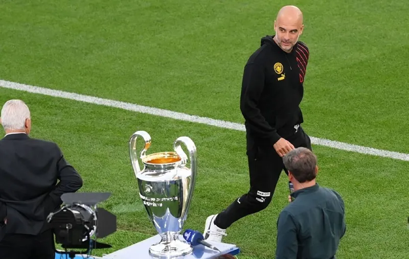 HLV Pep Guardiola lướt qua chiếc cúp Champions League khi công tác tổ chức trận chung kết đang diễn ra.