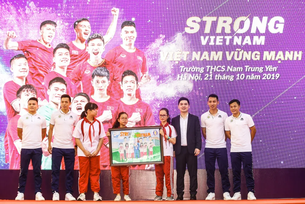 Các cầu thủ CLB bóng đá Hà Nội và Trưởng Ban tổ chức chương trình “Strong Vietnam” Đỗ Vinh Quang nhận quà là bức tranh từ các em học sinh THCS Nam Trung Yên