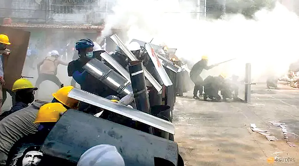 Người biểu tình ở Yangon che chắn đạn khói bằng các tấm khiên.  Ảnh: REUTERS