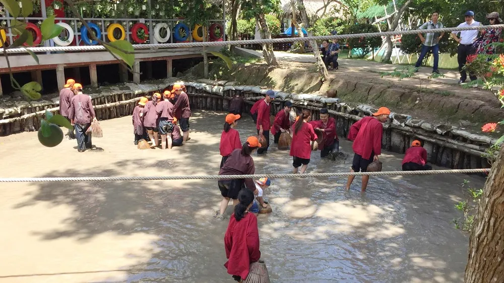 Khách du lịch trải nghiệm việc lội bùn bắt cá