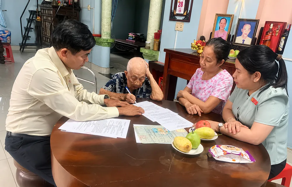 Công chức Trung tâm Phục vụ hành chính công xã Hóc Môn hỗ trợ cụ Lê Thị Tỷ thực hiện thủ tục hành chính tại nhà. Ảnh: HỮU TÂM