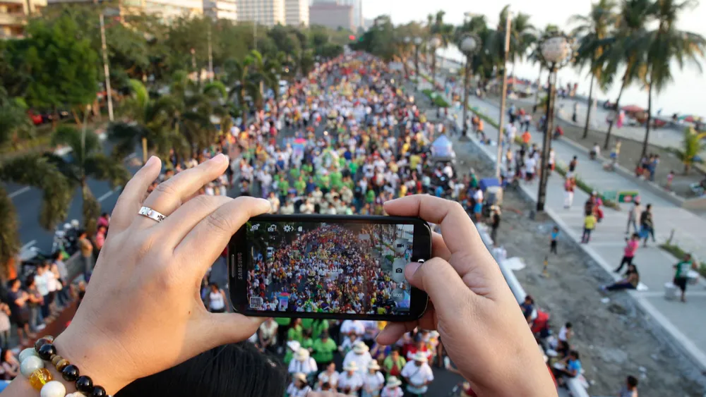 A person uses her cellphone to photo the procession by thousands of devotees to celebrate the feast day of the Child Jesus in Manila, Philippines. A consortium led by the parent of China Telecom has been granted a license to run the Philippines' third tel
