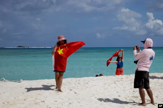 Chinese tourists take souvenir photos with the Chinese national flag as they visit Quanfu Island, one of Paracel Islands, on September 14, 2021. (Peng Peng/AP)