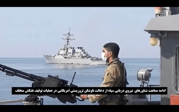 This frame grab from a video released by Iran’s paramilitary Revolutionary Guard on Wednesday, Nov. 3, 2021, shows a Guard soldier on a speed boat in front of a U.S warship amid the seizure of a Vietnamese-flagged oil tanker in the Gulf of Oman.