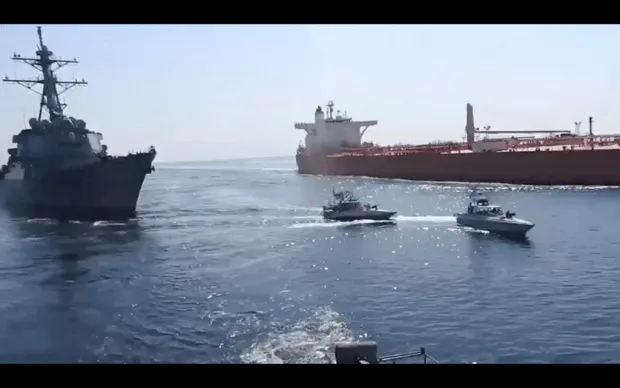 This frame grab from a video released by Iran’s paramilitary Revolutionary Guard on Wednesday, Nov. 3, 2021, shows the Guard speed boats, center, in front of a U.S warship, left, amid the seizure of a Vietnamese-flagged oil tanker, right, in the Gulf of Oman.