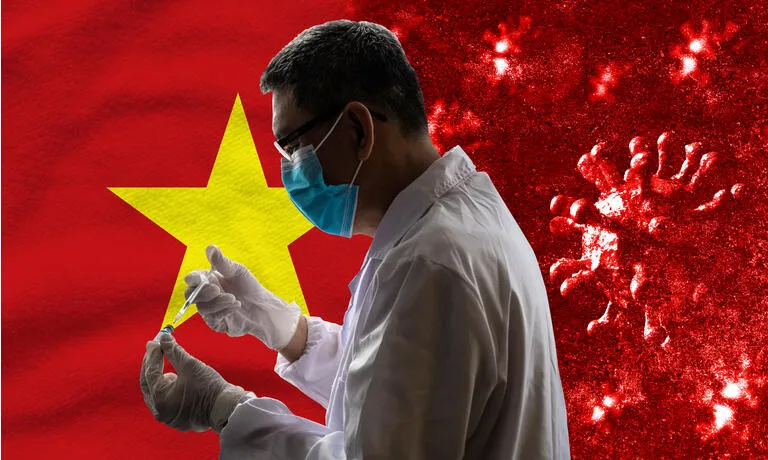 Doctor with protective facemask and wearing surgical gloves holding a syringe of Covid-19 vaccine against Vietnamese Flag background.