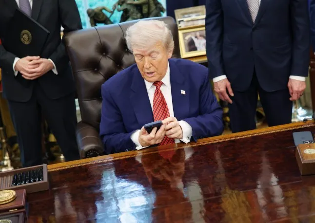 Tổng thống Donald Trump cầm iPhone trong buổi ký lệnh hành pháp tại Phòng Bầu dục của Nhà Trắng vào tháng 5 (Ảnh: Getty Images)