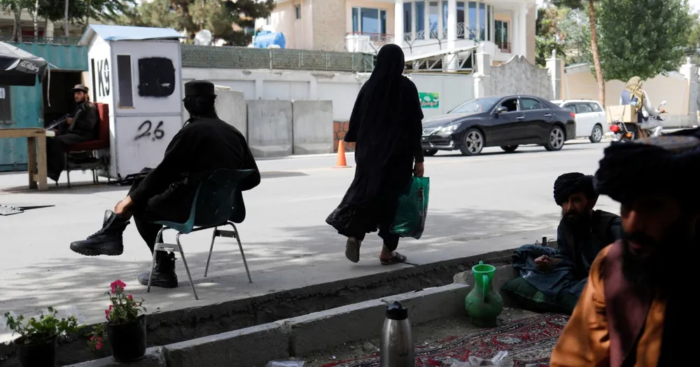 Một phụ nữ Afghanistan đi giữa những người lính Taliban tại một trạm kiểm soát ở Kabul, Afghanistan, ngày 6-7-2023.