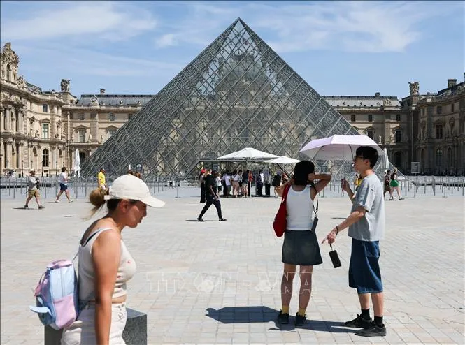 Du khách che ô chống nắng khi tham quan viện bảo tàng Louvre ở Paris, Pháp ngày 25-6. Ảnh: THX/TTXVN