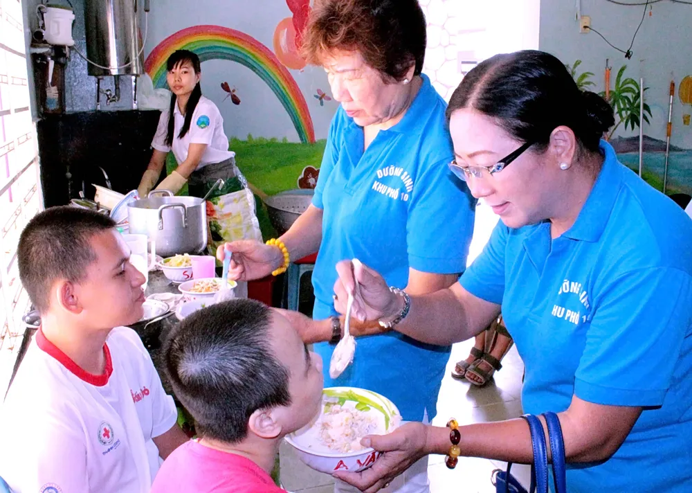 Chị Phạm Ngọc Dung (bìa phải) đến thăm, tặng quà, chăm sóc trẻ em tại Trung tâm Bảo trợ trẻ tàn tật, mồ côi Thị Nghè (TPHCM). Ảnh: MINH THANH